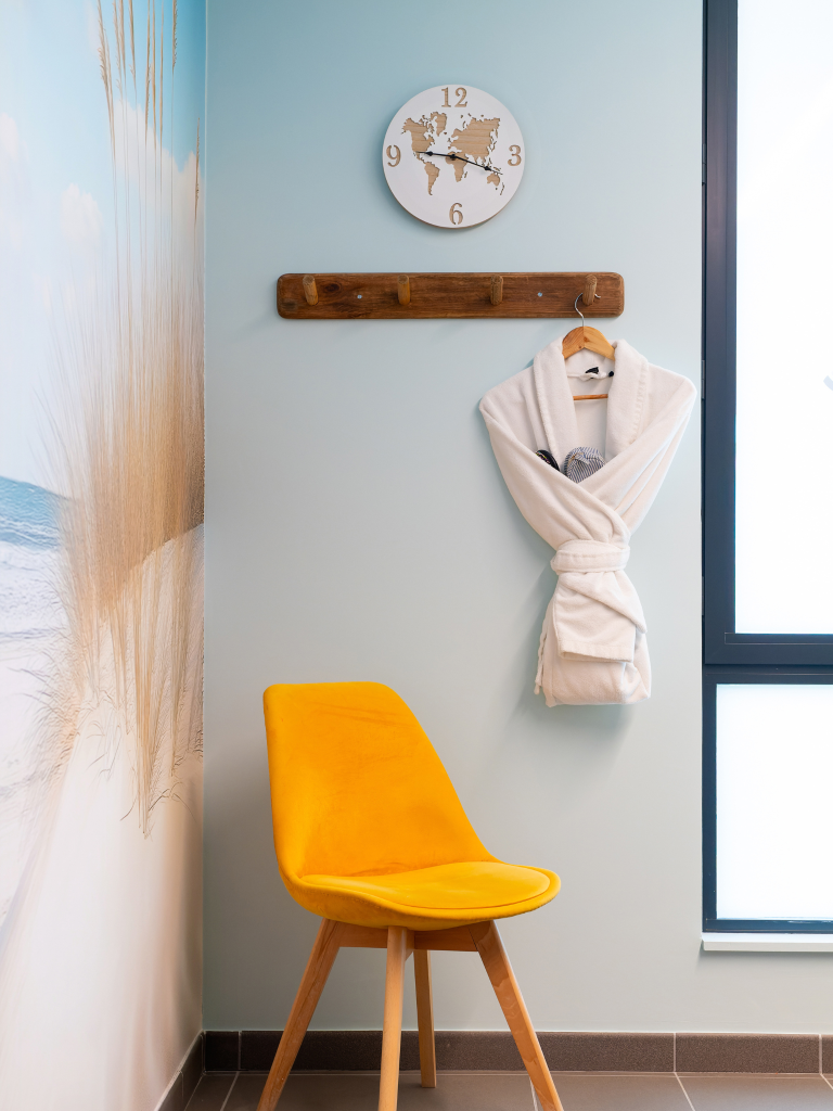 4. Siège jaune dans une salle de bain pour bébé avec horloge murale en forme de carte du monde et peignoir blanc accroché, ambiance chaleureuse et accueillante pour spa bébé Hauméa.