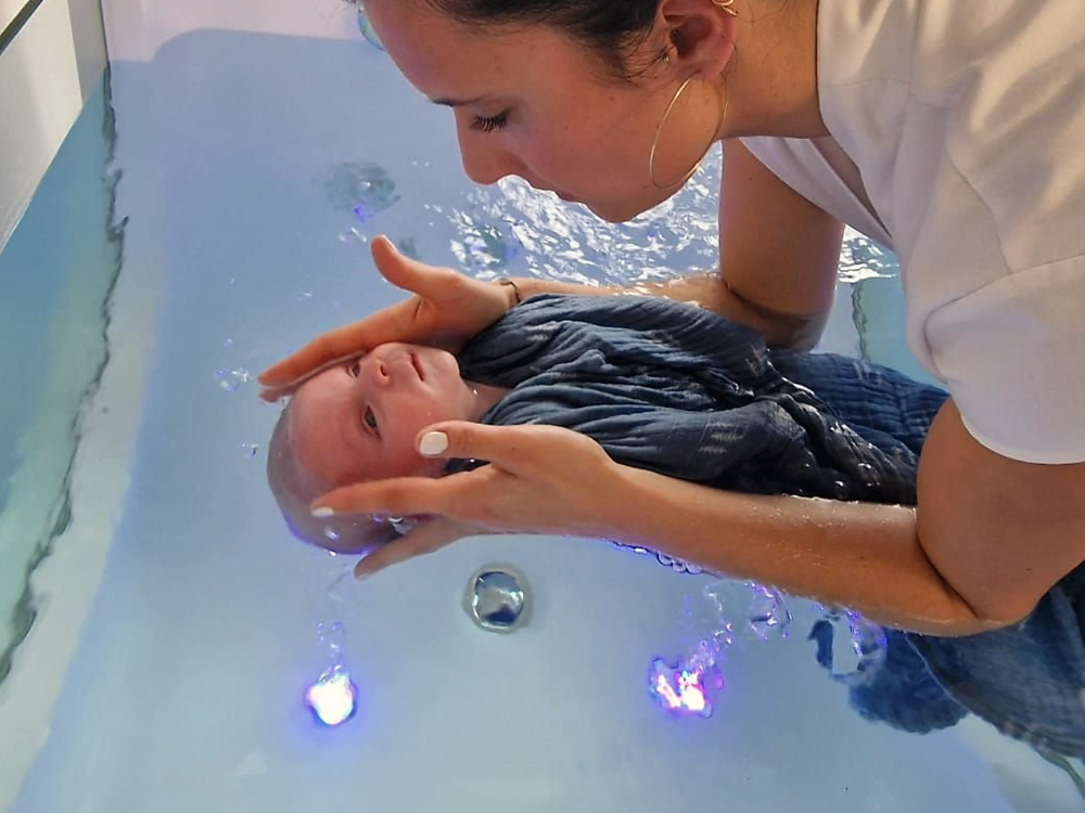 Les mains de la praticienne guident bébé dans l'eau